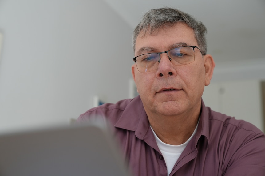 A man looking at his lapop and is wearing a purple button up shirt and glasses
