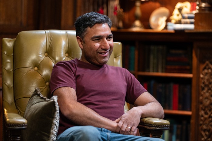 534675,TITLE:The Celebrity Traitors Nick Mohammed wearing a red top and blue jeans, smiling ahead.