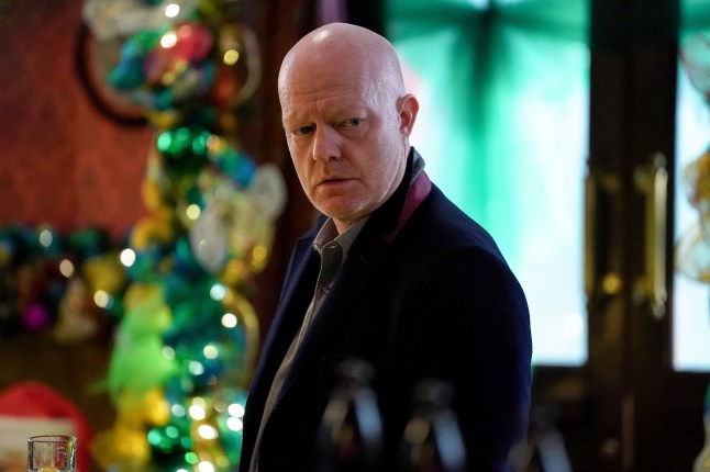 Max Branning standing at the Queen Vic bar in EastEnders, with Christmas decorations behind him.