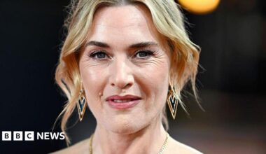 A head and shoulders image of actress Kate Winslet. She has short blonde hair and is wearing a gold necklace.
