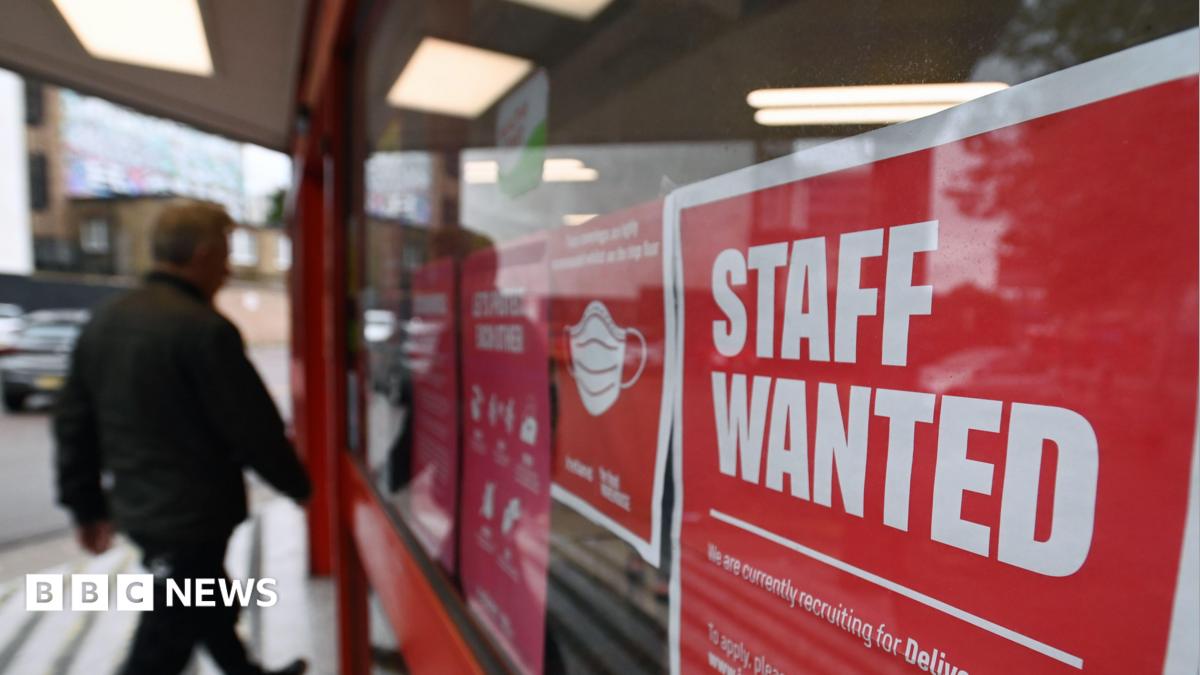 An image of a man walking past a red sign in a window saying staff wanted
