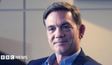 John Michie wearing a dark blue suit jacket and blue shirt. He has short dark hair.