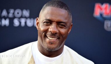 Luther Idris in a cream jacket and white T-shirt