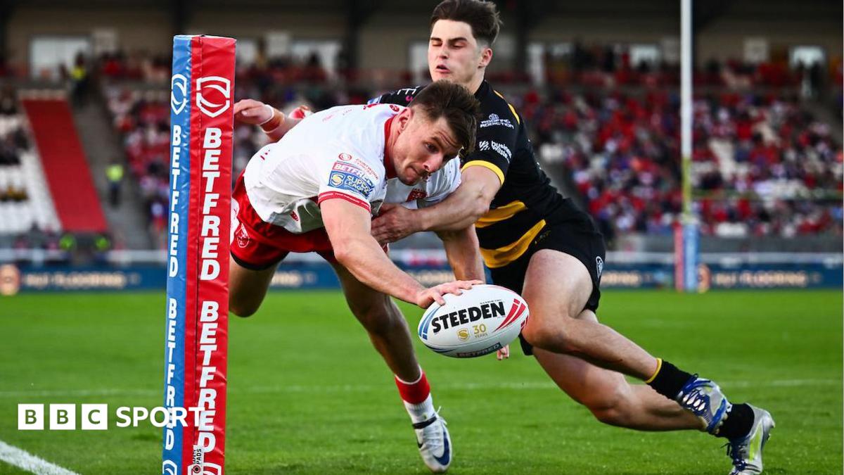 Hull KR winger Tom Davies reaches out with the ball in one hand as he dives towards the line under a challenge from a York Knight player