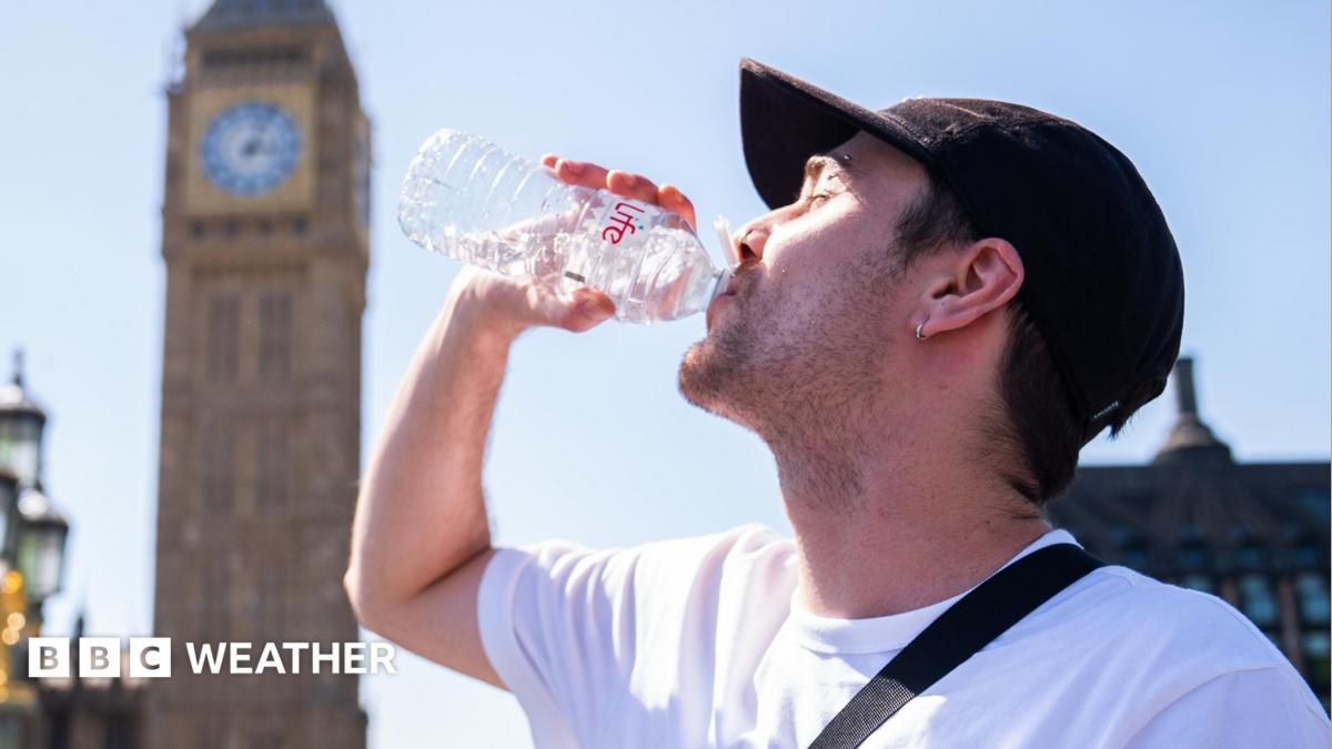 A man drinks from a water bottle with a sunny sky overhead and a blurred view of the Westminster skyline in the background