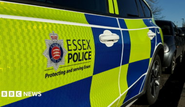 A Essex Police car parked. It has yellow and blue blocks of colour and the force logo on the side.