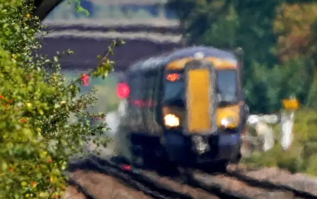 A train is out of focus as it passes through heat haze on a railway line. It is a small train with a flat front end. It is yellow and black.