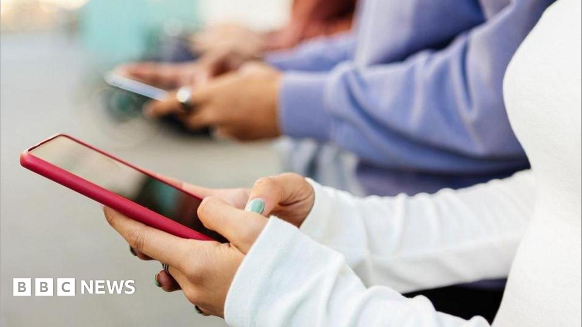 A close-up image of several young people using smartphones that appears to be indoor. The background is softly blurred, emphasising the hands and devices in the foreground.