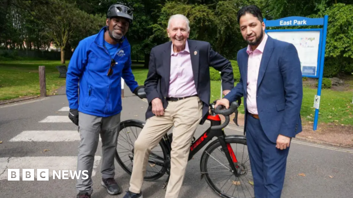 Three men, one seated on a stationary bike smile at the camera.