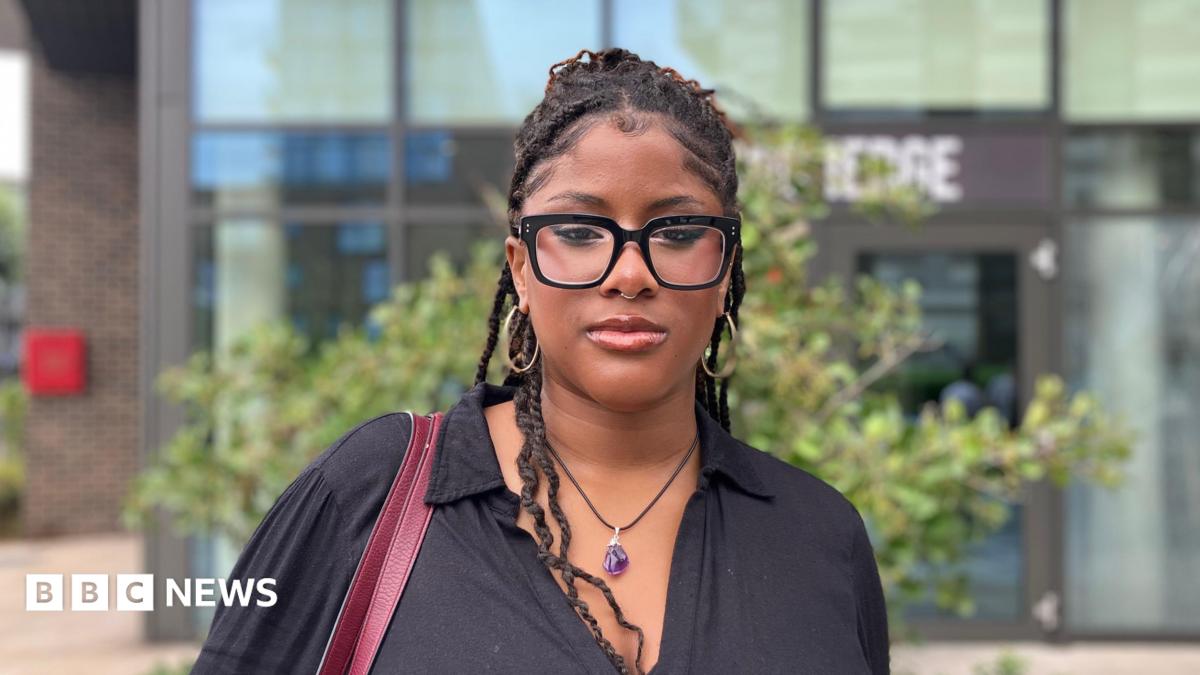 Mide Awosika wears glasses and a black shirt and is looking at the camera