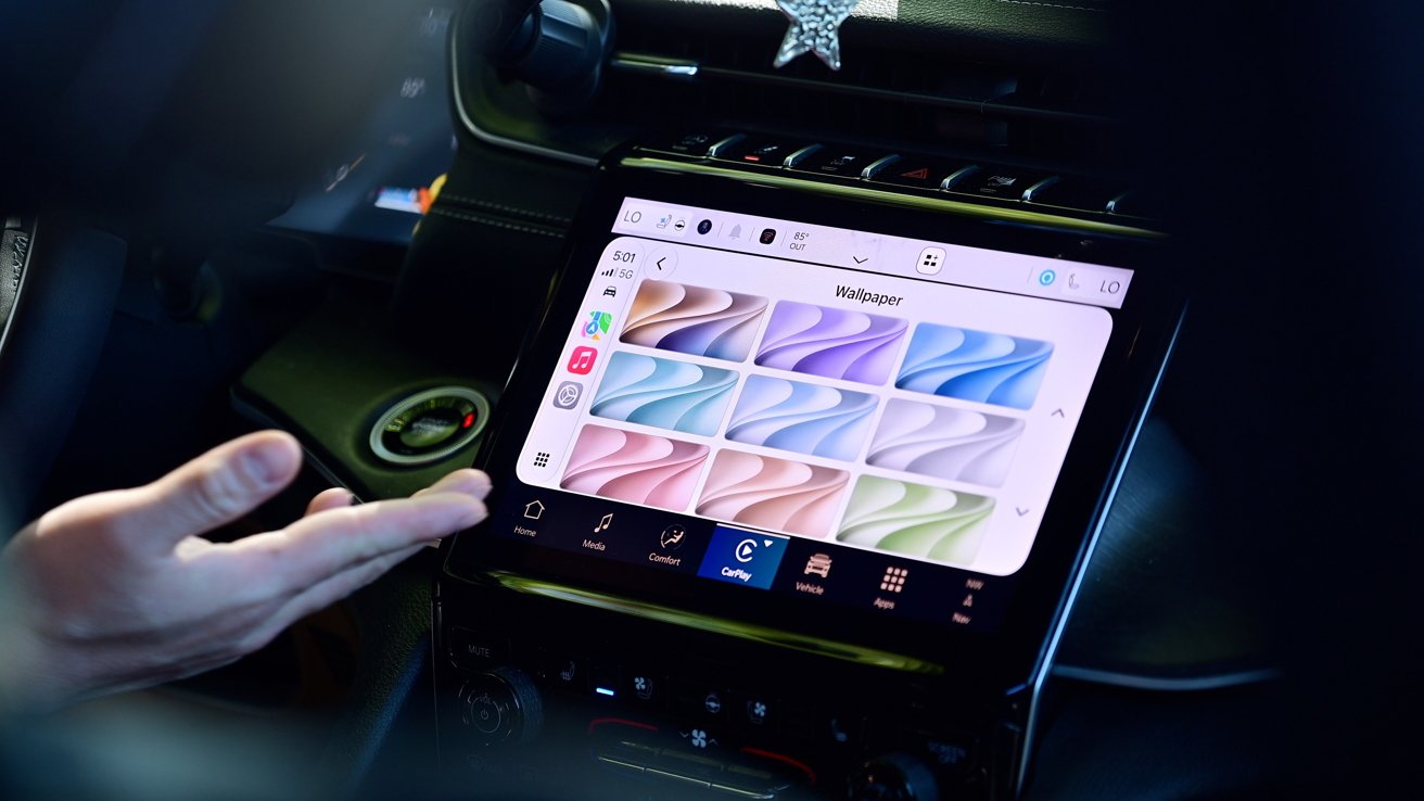 Person's hand gesturing toward a car's central touchscreen displaying a wallpaper selection menu with colorful abstract backgrounds, icons on the left side, and dashboard controls surrounding the screen