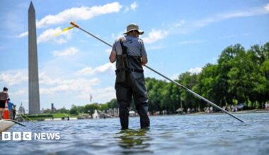 A worker in waders seen using a long pole to clean the pool