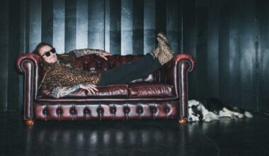 Ginger Wildheart lying on a chesterfield sofa, with his dog lying on the floor beside it
