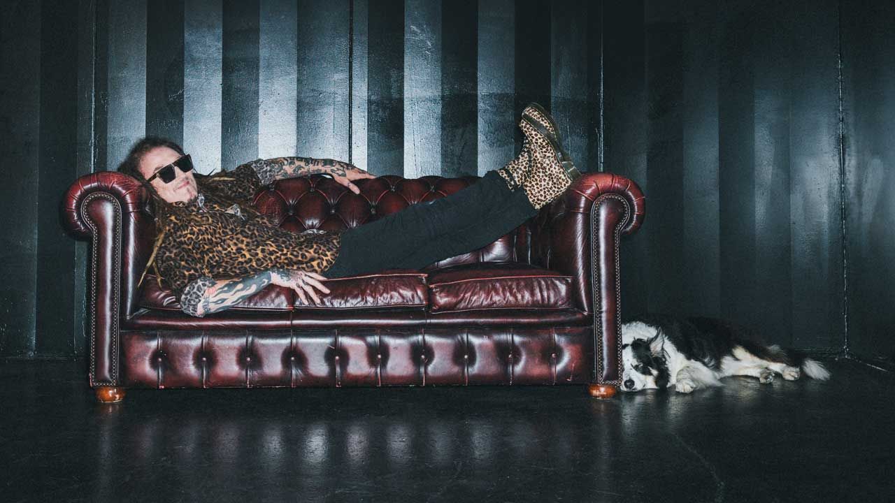 Ginger Wildheart lying on a chesterfield sofa, with his dog lying on the floor beside it