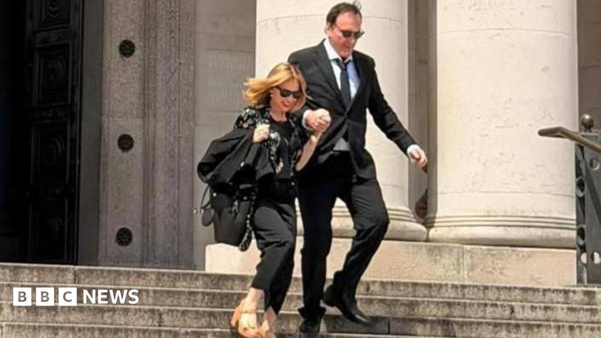 Quentin Tarantino and Kylie Minogue outside National Museum Cardiff. They are walking down the steps outside the museum holding hands. They are both wearing all black outfits and sunglasses. Kylie has a pair of brown tan high heels on.