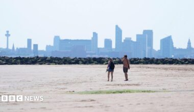Two people walking on New Brighton Beach on The Wirral, Merseyside. The Liverpool waterfront and skyline is in the distance.
