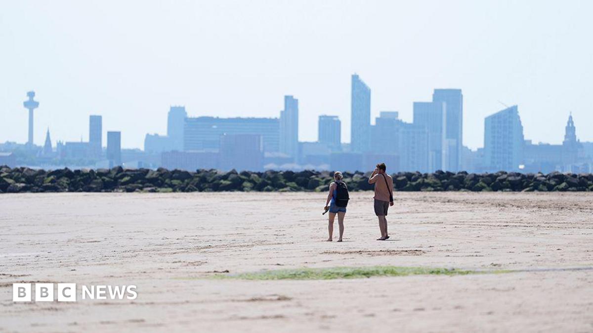 Two people walking on New Brighton Beach on The Wirral, Merseyside. The Liverpool waterfront and skyline is in the distance.