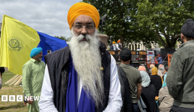 A Sikh man wearing an orange turban at a march in London. He is looking into the camera.