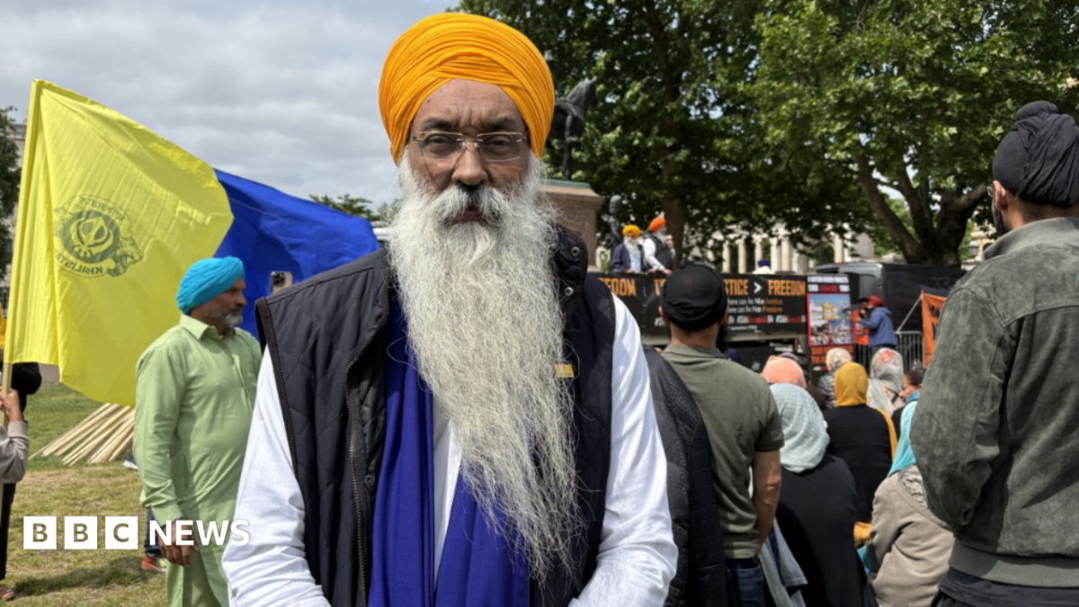 A Sikh man wearing an orange turban at a march in London. He is looking into the camera.