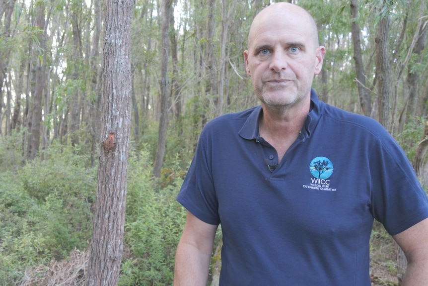 Shaun Ossinger wears a blue t-shirt, trees in the background.