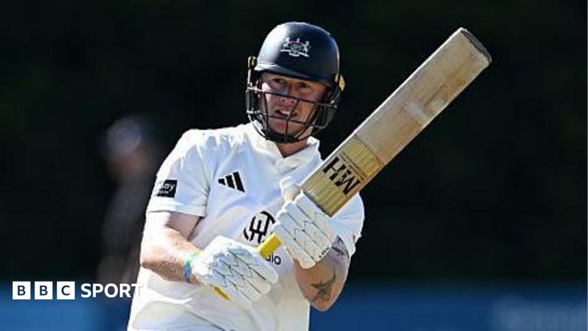 Miles Hammond pulls the ball away through mid-wicket. He is holding his bat high to the right of the picture. He is wearing his whites and has a dak blue helmet on