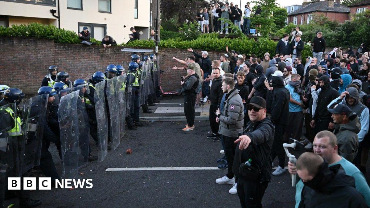 A line of riot police face off against a large group of protestors in the middle of a road.