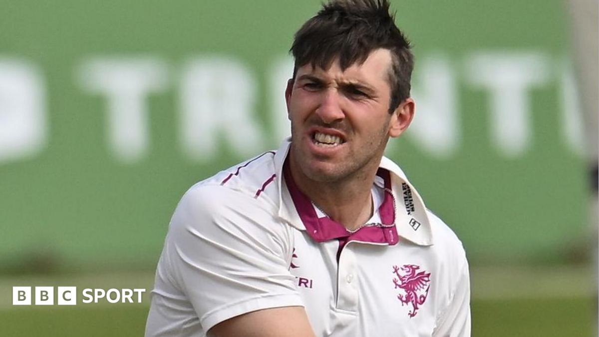 Craig Overton wearing a white Somerset shirt grits teeth