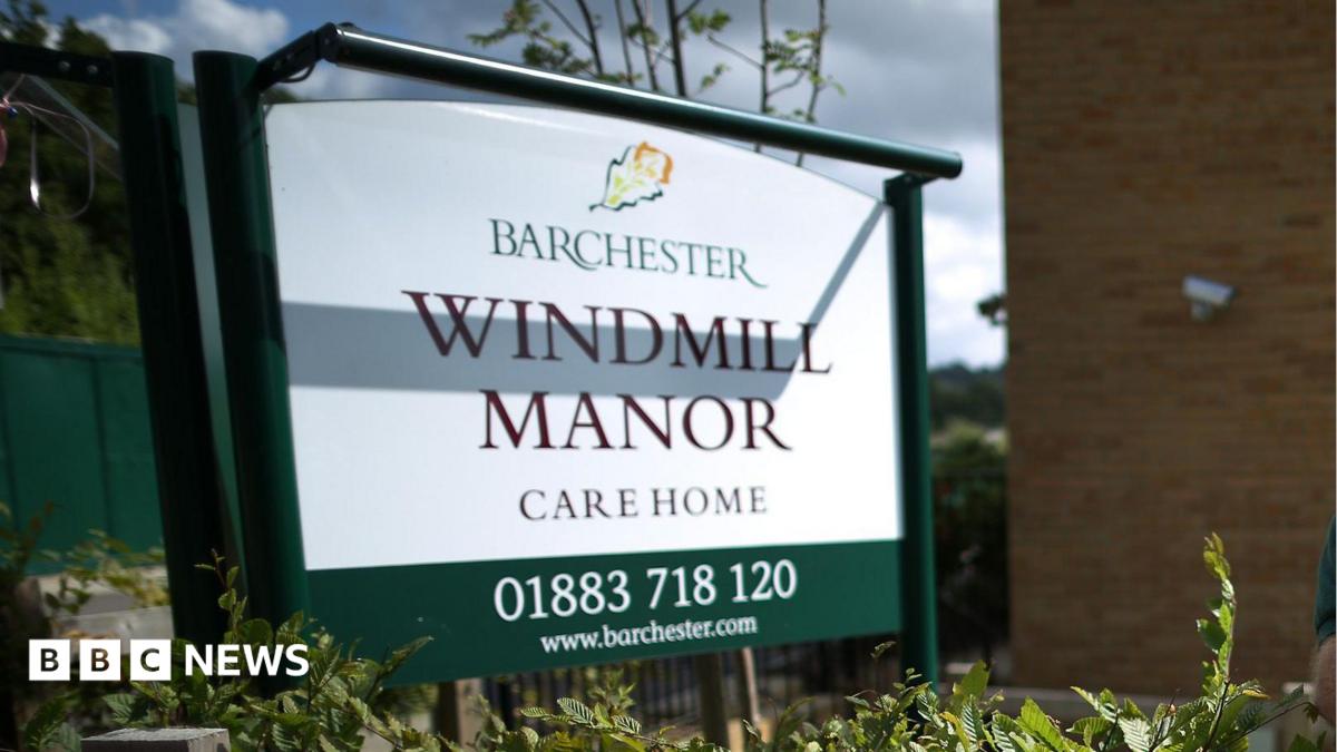 A white sign outside a building reading BARCHESTER WINDMILL MANOR CARE HOME 01883 718 120