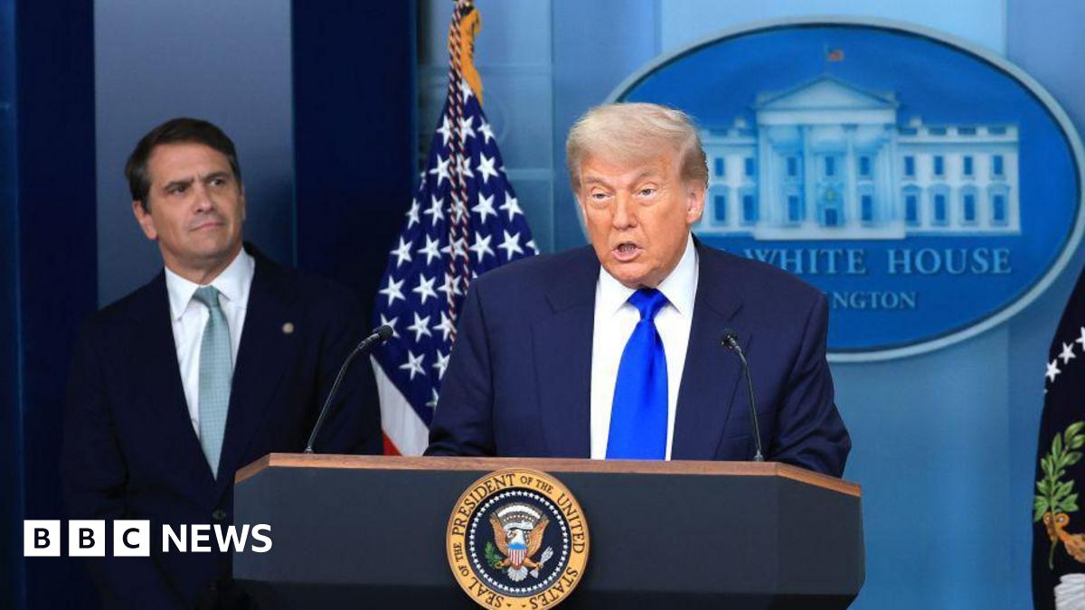 Trump is at the podium and speaking while wearing a dark blue suit and bright blue tie. To his right and behind him is Todd Blanche who is wearing a dark suit and indigo tie