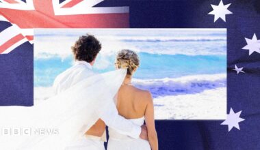 A newlywed couple are seen looking out to sea on a beach, with a photo of the Australian flag in the background.