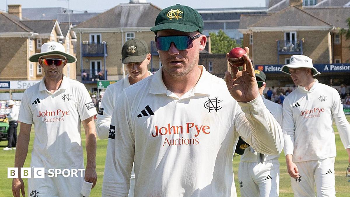 Liam Patterson-White holds up a red cricket ball with players surrounding him