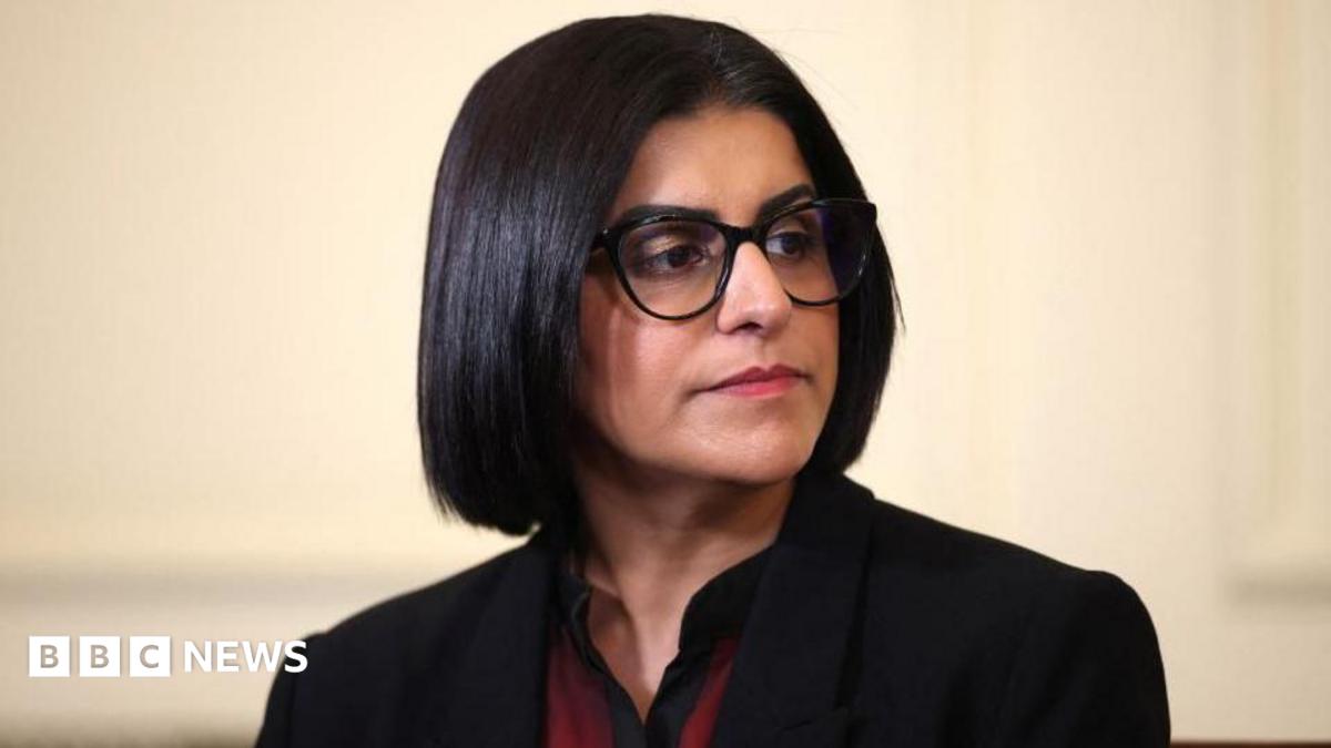Home Secretary Shabana Mahmood is pictured looking off camera. She is wearing a dark jacket with a red and black top on beneath.