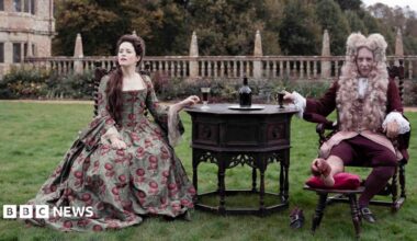 Claire Foy and Richard E Grant starring in Savage House sit on a lawn in front of Montacute House in Somerset wearing period dress.