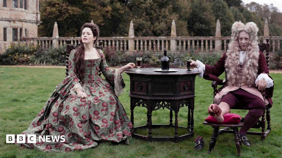 Claire Foy and Richard E Grant starring in Savage House sit on a lawn in front of Montacute House in Somerset wearing period dress.