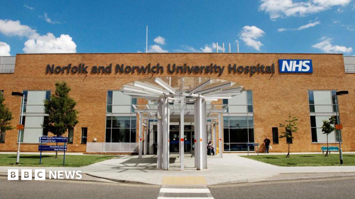 The refurbished outpatients' entrance at the Norfolk and Norwich University Hospital. It shows a white revolving door to the front, with signage to the left and some trees and bushes outside.