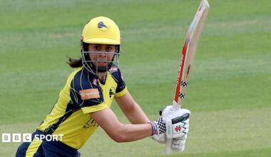 Hampshire's Maia Bouchier, wearing a yellow and blue kit and yellow cricket helmet, watches the ball to her right after playing a shot