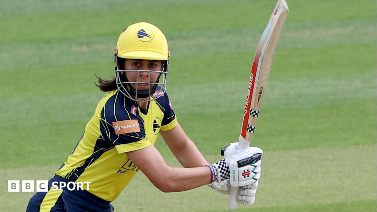 Hampshire's Maia Bouchier, wearing a yellow and blue kit and yellow cricket helmet, watches the ball to her right after playing a shot
