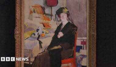 An oil painting of a woman wearing black sitting on a chair. There are other pieces of furniture in the background. The painting is framed and hung on a black wall.