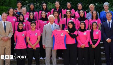 Members of the Afghanistan women's cricket team pose with King Charles, who is holding a signed shirt