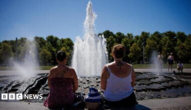 Two women look at a fountain on a sunny day with their backs to the camera