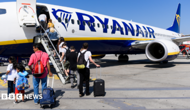 Passengers incluidng children boarding a Ryanair aircraft using the steps at the front of the plane on a sunny day with blue skies