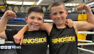 Photo of Jake and Tommy in front of the boxing ring with their arms round each other. They are smiling and wearing black Bristol Ringside tops.