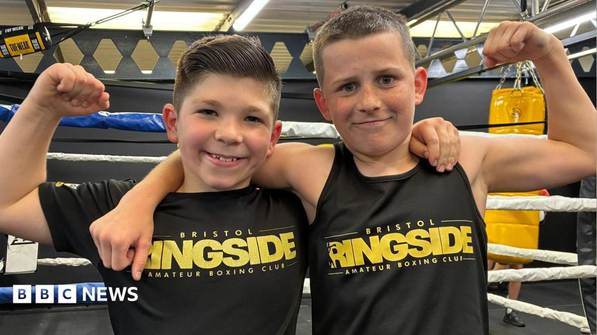 Photo of Jake and Tommy in front of the boxing ring with their arms round each other. They are smiling and wearing black Bristol Ringside tops.