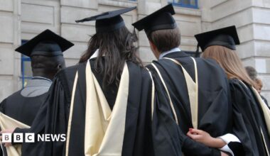 Four students dressed in graduation robes and mortarboards stand with their backs to the camera.