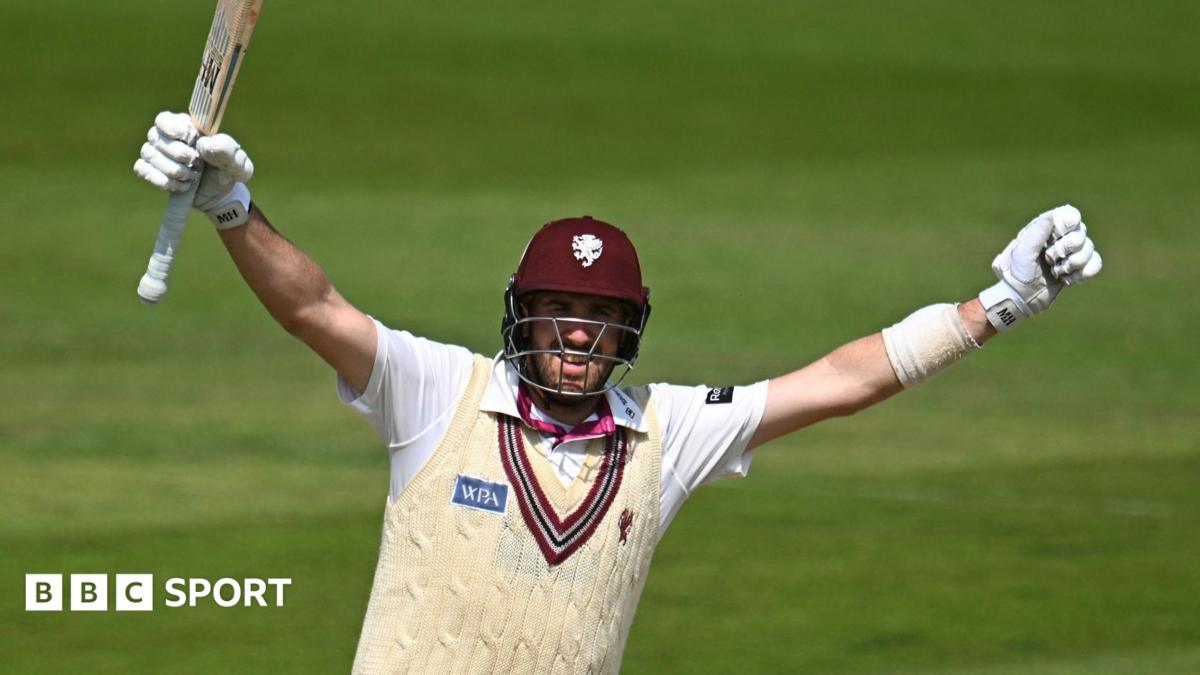 Craig Overton, with arms outstretched and bat raised, celebrates reaching a century for Somerset