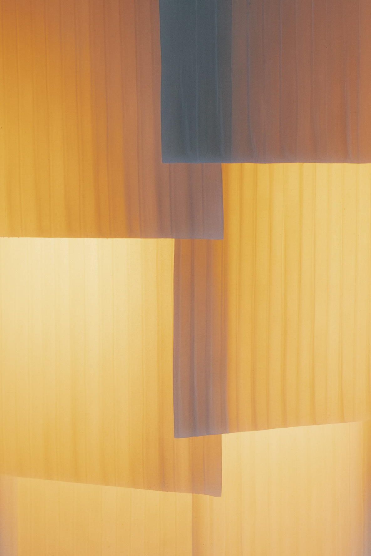 A multilayered table lamp made of overlaid fabric sheets in a stripy motif, captured up close when turned on.