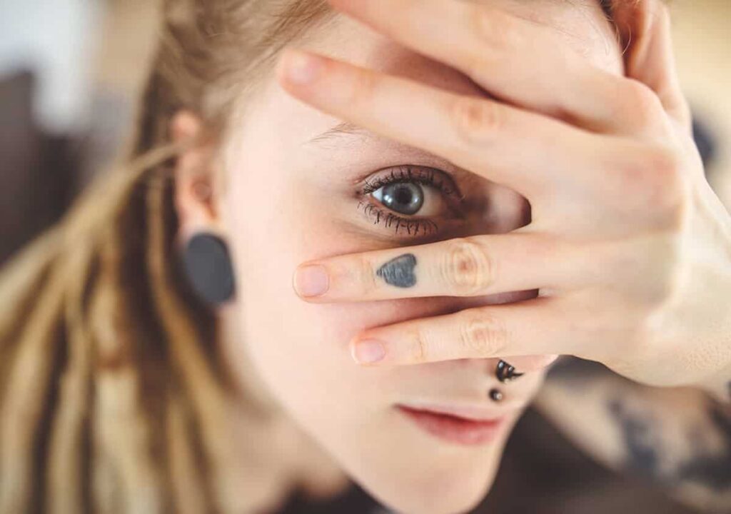 Close-up of a young woman with blue eyes covering part of her face with her hand.