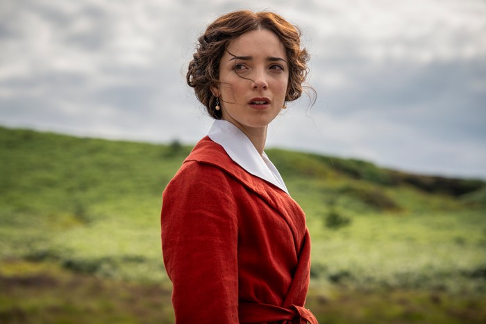 A Woman of Substance Ep7 Jessica Reynolds as Emma Harte in A Woman of Substance standing on top of a hill, looking worried as she wears a red blazer and white shirt.