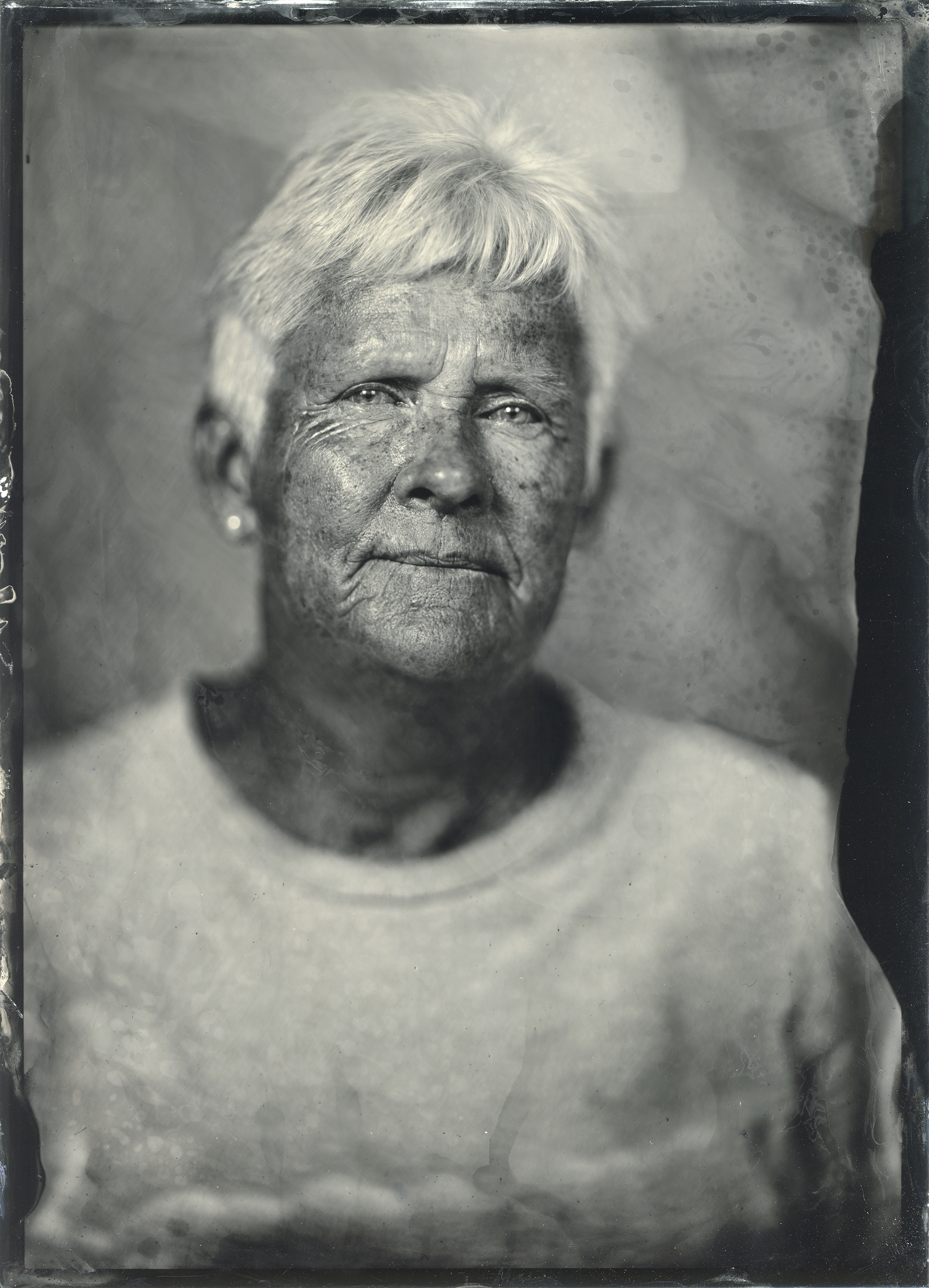 A wet-plate collodion tintype portrait of an older white-haired woman, her weathered face rendered in deep tones with the characteristic texture and dark border of the nineteenth-century process.