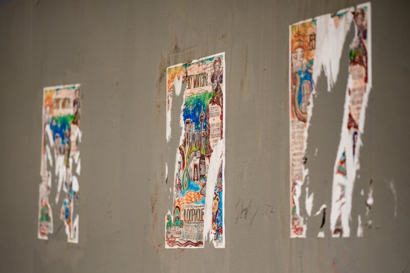 Three colorful posters are partially torn and peeling off a gray wall, leaving only fragments and faded images visible.